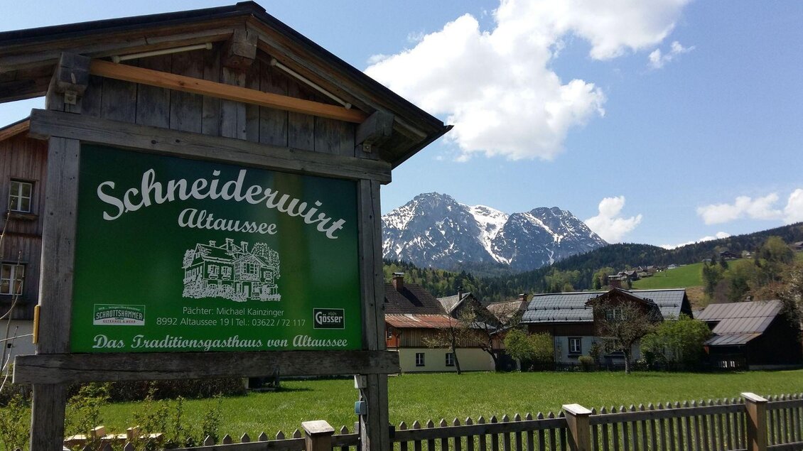 Ein traditionelles Gasthaus mit dem Namen "Schneiderwirt" in Altaussee. Im Hintergrund sind schneebedeckte Berge und ein klarer Himmel zu sehen. | © Petra Kirchschlager