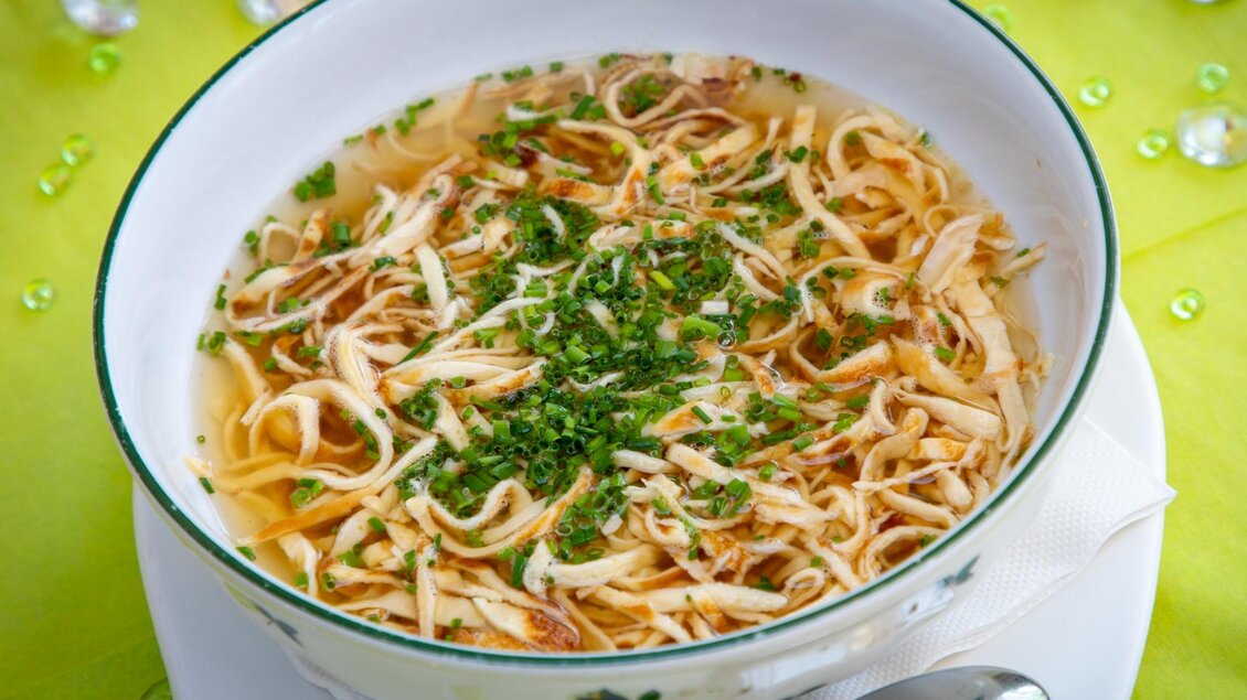 Eine Schüssel mit schmackhafter Hühnersuppe, garniert mit frischen Kräutern. Im Hintergrund steht eine kleine Vase mit einem Zweig. | © TV Region Graz - Lunghammer