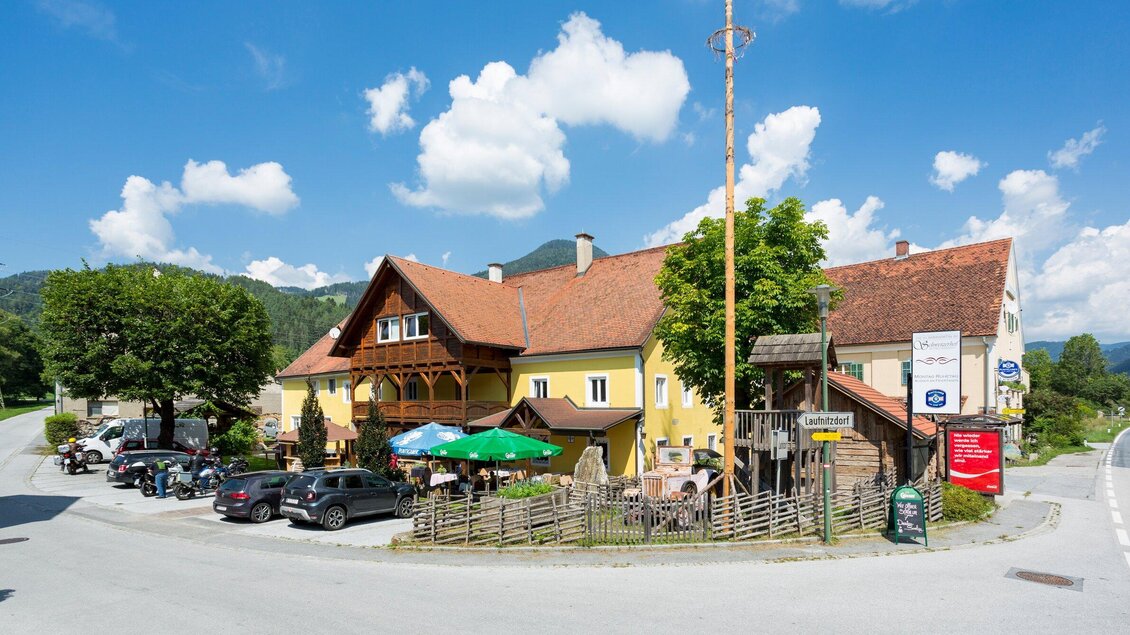 Ein gemütliches Gasthaus mit braunem Dach und grünen Markisen. Umgeben von Bäumen und einem klaren blauen Himmel. | © TV Region Graz - René Vidalli