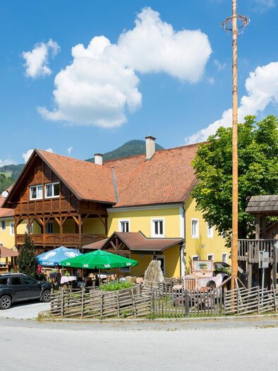 Ein gemütliches Gasthaus mit braunem Dach und grünen Markisen. Umgeben von Bäumen und einem klaren blauen Himmel. | © TV Region Graz - René Vidalli