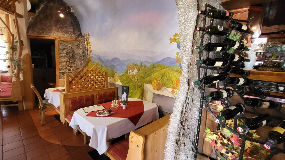 Ein gemütliches Restaurant mit Holzdekor und gedeckten Tischen. An der Wand ist ein malerisches Landschaftsmotiv zu sehen, und ein Weinständer steht im Vordergrund.