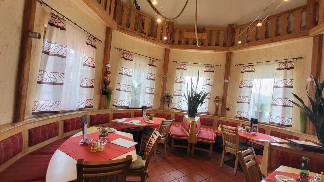 Ein gemütliches Restaurant mit runden Tischen und roten Sitzbänken. Große Fenster sorgen für helle Beleuchtung und eine einladende Atmosphäre. | © TV Hochsteiermark