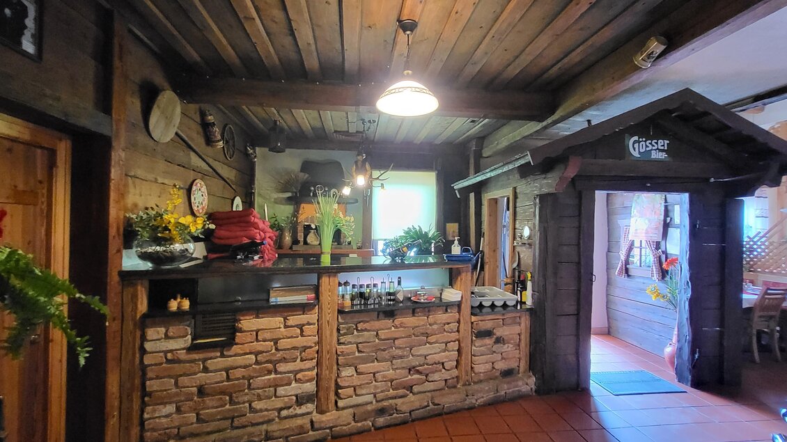 Ein gemütlicher Innenraum mit einer Steinbar und Holzbalkendecke. Der Eingang zu einem weiteren Raum ist sichtbar, mit dekorativen Elementen und Lichtquellen. | © TV Hochsteiermark