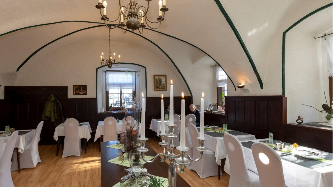 Ein gemütliches Restaurant mit hellen Wänden und Holzboden. Es sind Tische mit weißen Tischdecken und künstlerischen Bildern an den Wänden zu sehen. | © TV Region OberGraz - Lunghammer