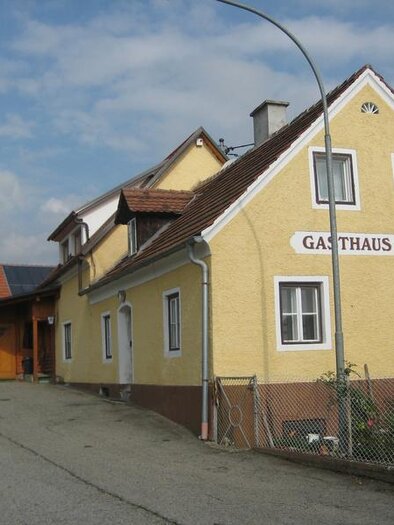 Ein gelbes Gasthaus mit einem einladenden Eingangsbereich. Die Straße ist ruhig und gepflastert, umgeben von einer grünen Landschaft. | © Erlebnisregion Murtal