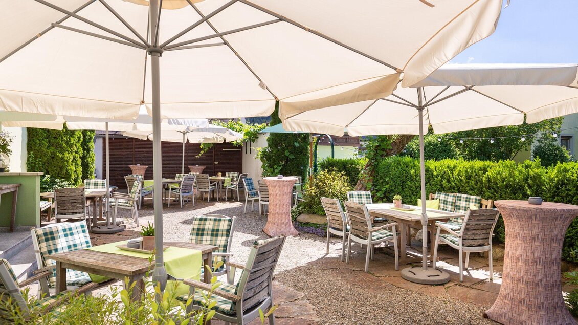 Ein einladender Außenbereich mit Sonnenschirmen und Tischen. Umgeben von grünen Pflanzen bietet er einen angenehmen Ort zum Entspannen. | © Geopho