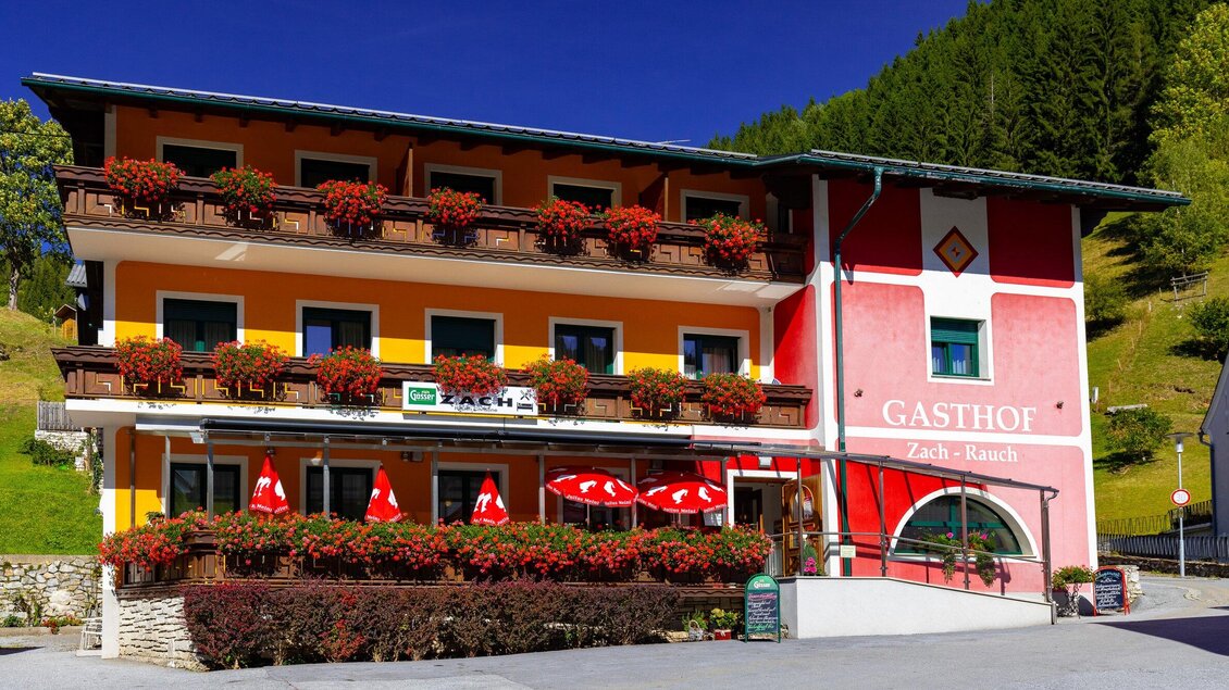 Ein charmantes Gasthaus mit bunten Fassaden und blühenden Blumenkästen. Außen gibt es rote Sonnenschirme, die einladend wirken. | © TV Region Graz-Harry Schiffer