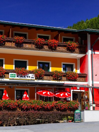 Ein charmantes Gasthaus mit bunten Fassaden und blühenden Blumenkästen. Außen gibt es rote Sonnenschirme, die einladend wirken. | © TV Region Graz-Harry Schiffer