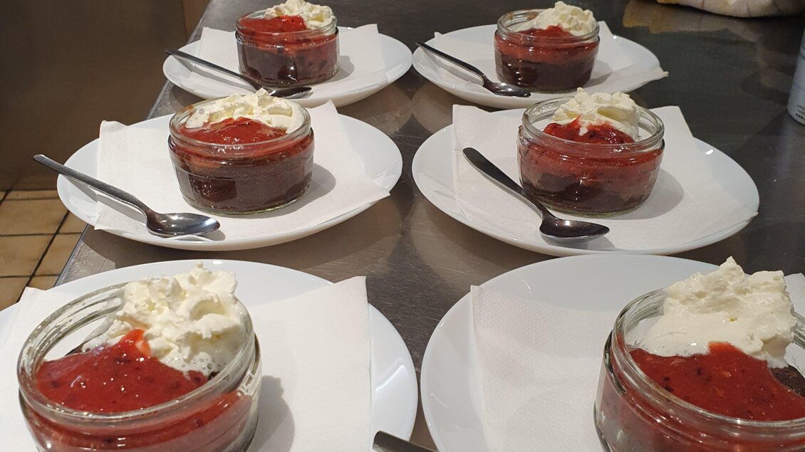 Sechs Gläser mit Dessert auf weißen Tellern, garniert mit Sahne und fruchtiger Soße. Im Hintergrund sind Kochutensilien sichtbar. | © Emil