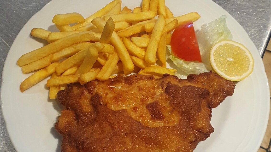 Ein Teller mit paniertem Schnitzel, Pommes frites und frischem Salat. Dazu gibt es eine Zitronenscheibe und eine Tomate. | © Emil 