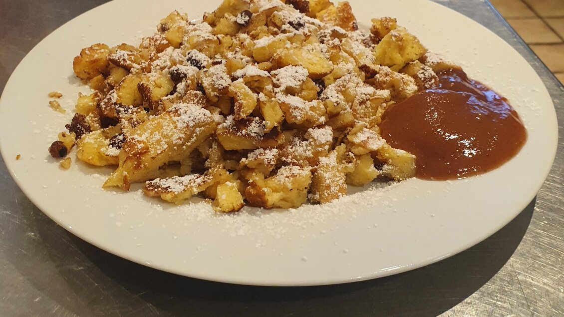 Ein Teller mit Kaiserschmarrn, bestreut mit Puderzucker und serviert mit Apfelmus. Das Gericht ist goldbraun und sieht lecker aus. | © Emil