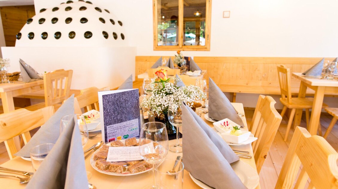 Ein gemütliches Restaurant mit Holztischen und eleganter Tischdekoration. Die Tische sind liebevoll mit Blumen und Menükarten eingedeckt. | © Region Graz - Harry Schiffer