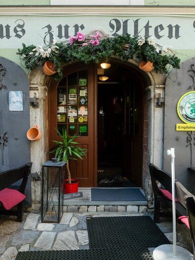 Ein gemütliches Gasthaus mit der Aufschrift „Gasthaus zur Alten Press“. Der Eingang ist mit Pflanzen und Dekoration geschmückt und es gibt Tische im Freien. | © Gasthaus zur Alten Press
