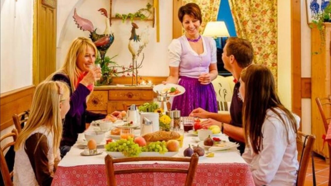 Ein gemütlicher Frühstückstisch mit mehreren Personen in traditioneller Kleidung. Die Atmosphäre ist freundlich und einladend, mit frischen Speisen und Getränken. | © Gasthof Bräuer