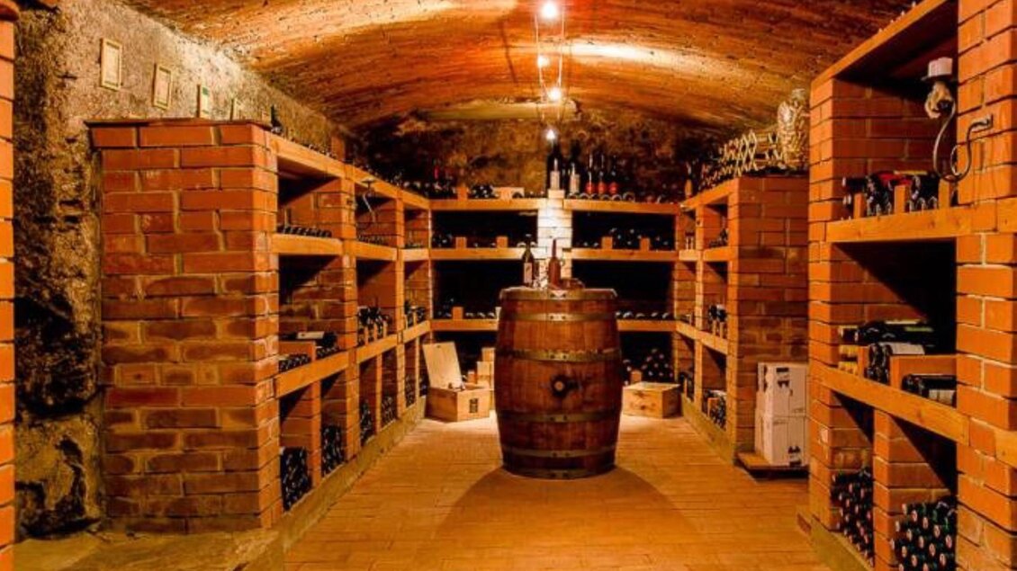 Ein Weinkeller mit roten Ziegelregalen und einem großen Holzfass in der Mitte. Die Wände sind aus Stein und die Beleuchtung ist warm und einladend. | © Gasthof Bräuer