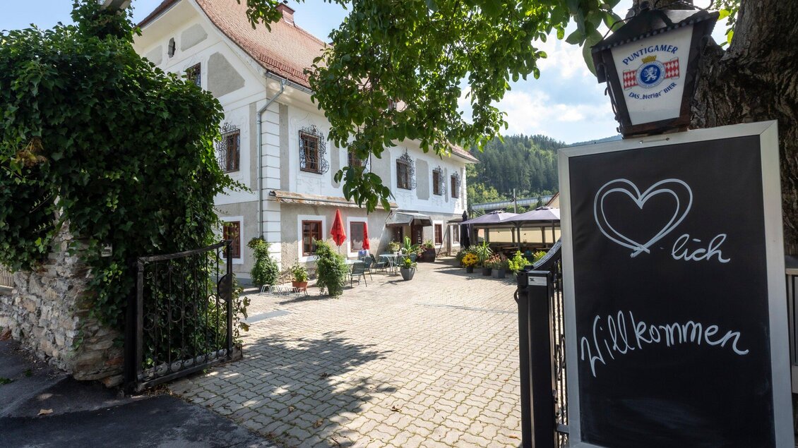 Ein einladendes Hotel mit schöner Fassade und bunten Blumen. Eine Tafel mit der Aufschrift "Willkommen" steht im Vordergrund. | © TV Region Graz - Lunghammer