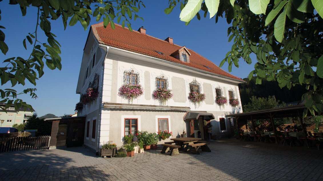 Ein charmantes Gebäude mit blühenden Fensterkästen und einem roten Dach. Der Außenbereich bietet Sitzgelegenheiten im Freien und ist von Bäumen umgeben. | © TV Region Graz - Lunghammer