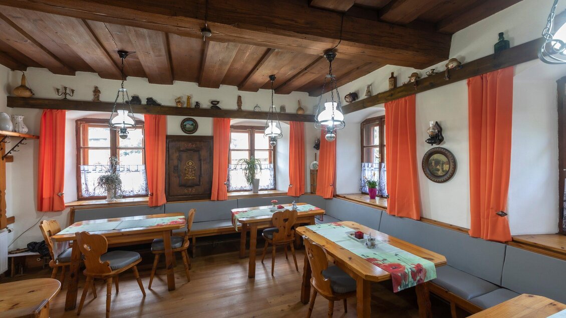 Ein gemütliches Restaurant mit Holztischen und -stühlen. Die Fenster sind mit orangefarbenen Vorhängen geschmückt, und es gibt dekorative Elemente an den Wänden. | © TV Region Graz - Lunghammer