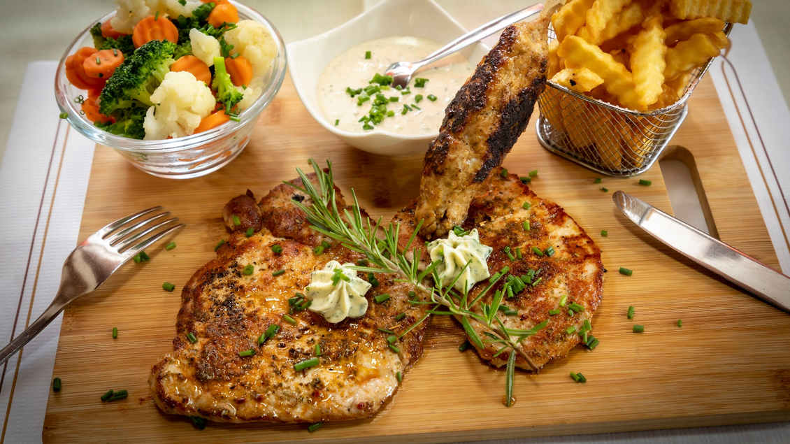 Ein köstliches Gericht mit zwei knusprigen Fleischstücken, garniert mit Kräutern und Sahne. Dazu gibt es Gemüse und Pommes frites in einem kleinen Korb. | © TV Region Graz - Lunghammer