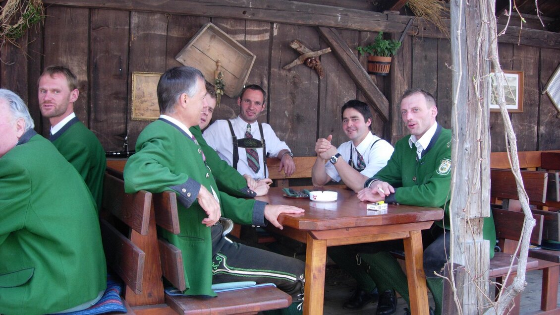 Eine Gruppe von Männern in traditionellen Trachten sitzt an einem Holztisch in einer gemütlichen Umgebung. Die Männer scheinen sich zu unterhalten und zu entspannen. | © Gasthof Angermaier - Winklwirt