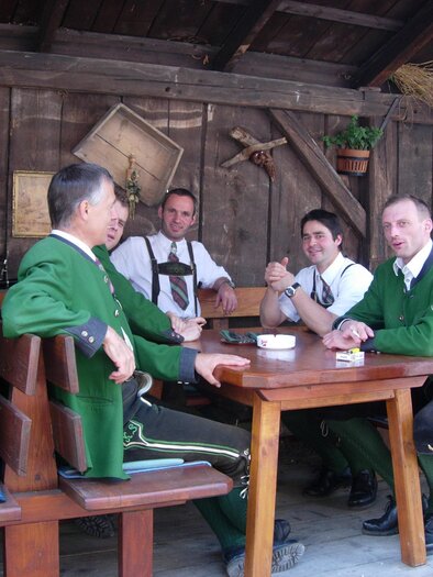 Eine Gruppe von Männern in traditionellen Trachten sitzt an einem Holztisch in einer gemütlichen Umgebung. Die Männer scheinen sich zu unterhalten und zu entspannen. | © Gasthof Angermaier - Winklwirt