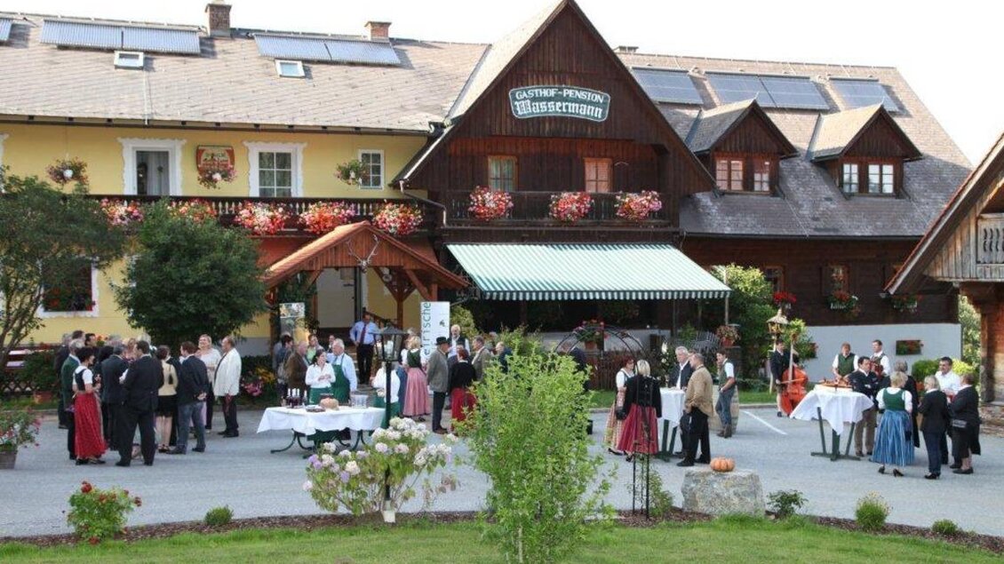 Eine Feier im Freien vor einem traditionellen Gasthaus. Viele Gäste in festlicher Kleidung genießen das Ambiente. | © Gasthof BIOALM Wassermann-Wirt