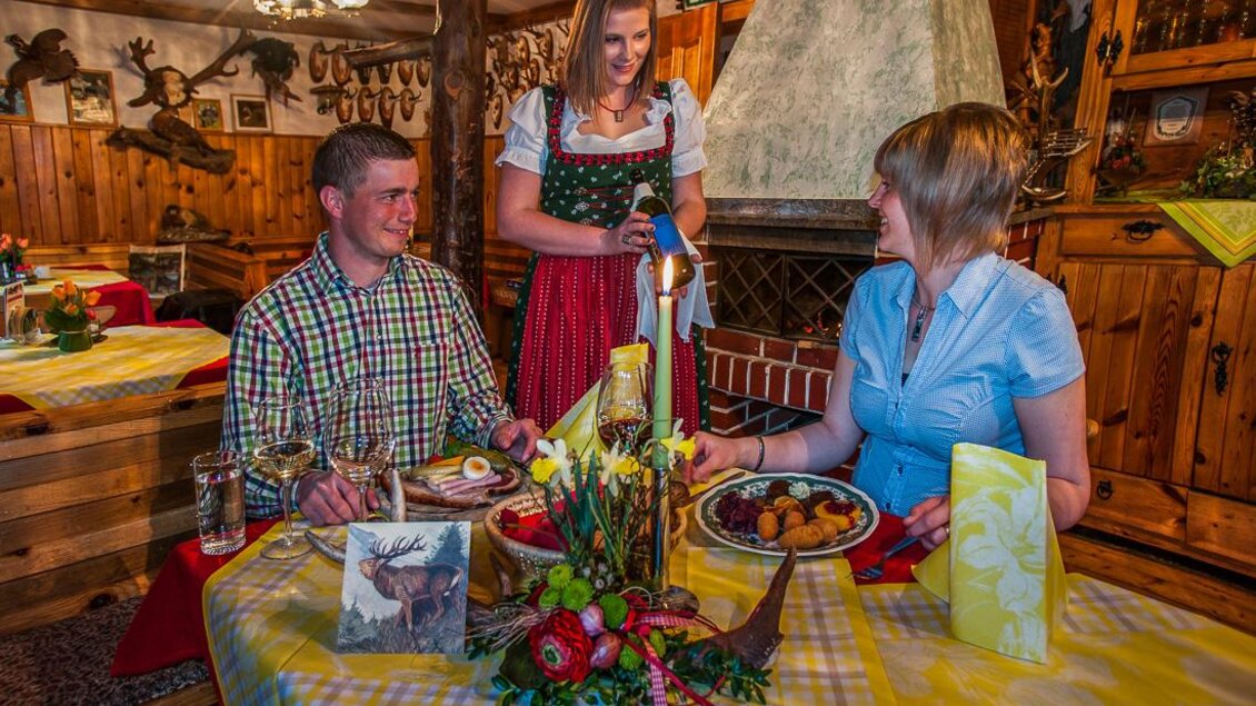 Eine gemütliche Restaurantatmosphäre mit zwei Gästen, die am Tisch sitzen und eine Kellnerin bedienen. Die Dekoration ist rustikal, mit Holz und traditionellen Elementen. | © Gasthof Beren "Jägerheim"