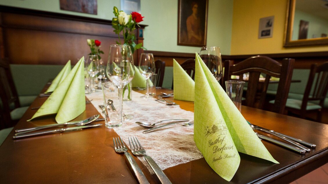 Ein schön gedeckter Tisch in einem Restaurant mit grünen Servietten und Gläsern. Auf dem Tisch steht eine kleine Blumenvase mit roten Rosen. | © TV Region - Mias Photoart