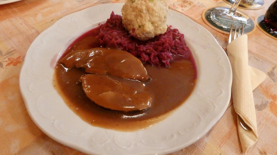 Ein herzhaftes Gericht mit Leber, serviert auf einem Bett aus Rotkraut und einer Knödel. Dazu eine dunkle Soße und ein elegantes Gedeck. | © Gasthof Franzbauer