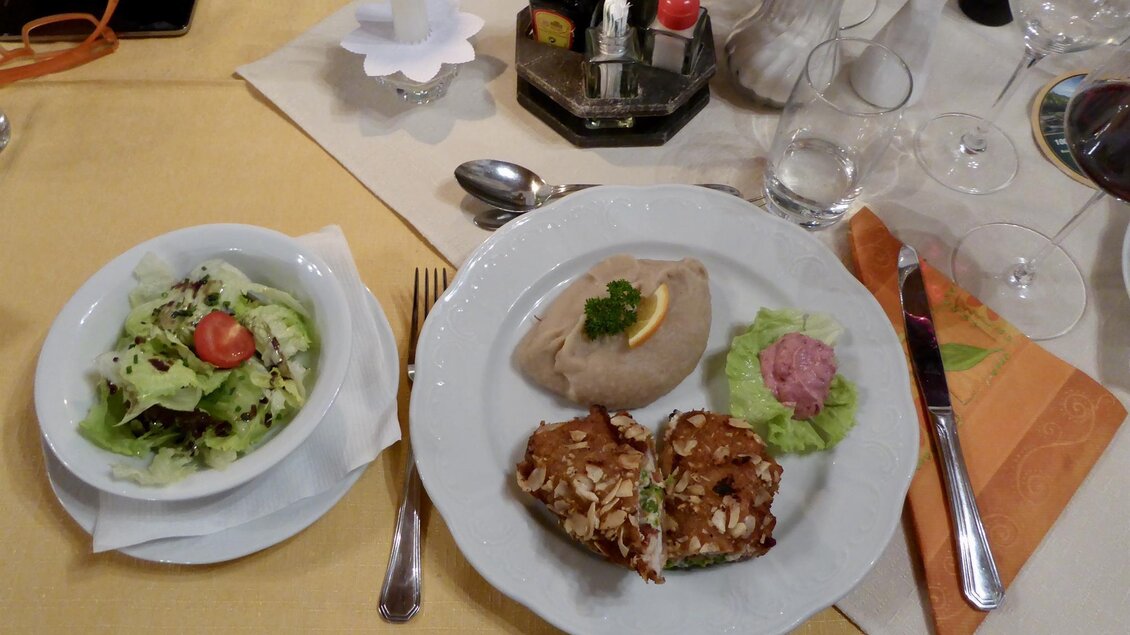 Ein Teller mit einer herzhaften Speise, die aus einer gefüllten Frikadelle und Beilagen besteht, sowie einem frischen Salat. Der Tisch ist gedeckt mit Besteck und anderen Tischdekorationen. | © Gasthof Franzbauer