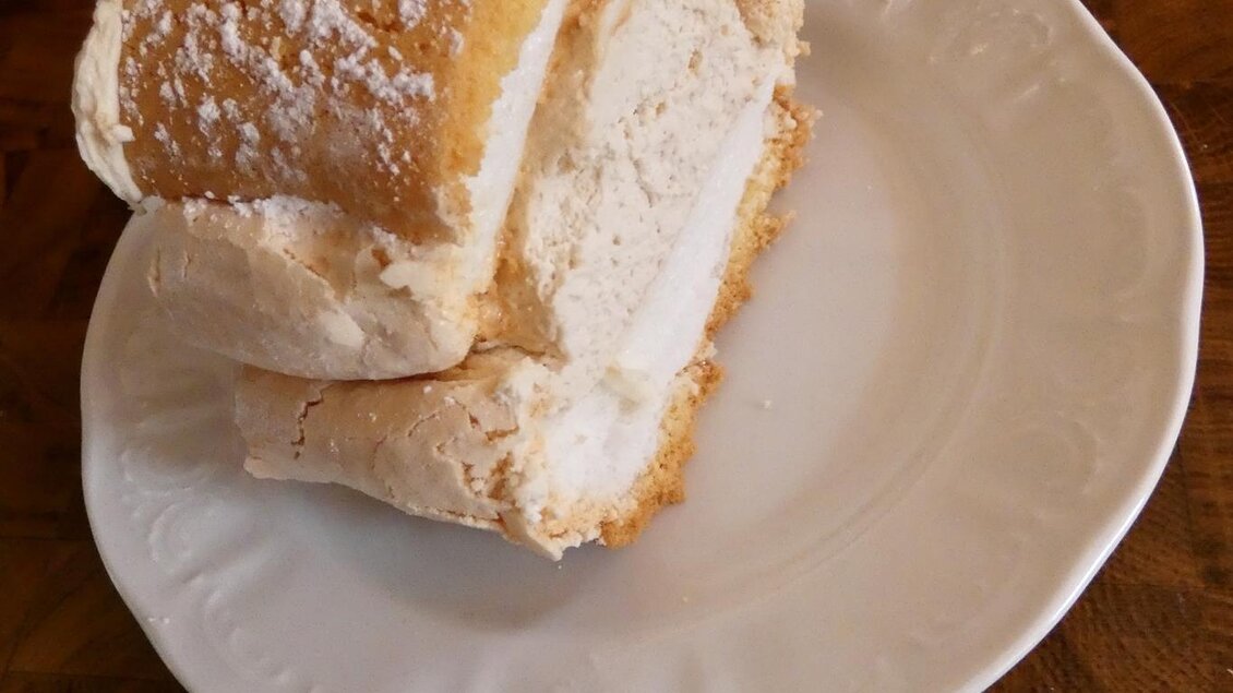 Ein Stück Kuchen auf einem weißen Teller, mit Puderzucker bestreut. Im Hintergrund sind weitere kleine Kuchen portioniert. | © Gasthof Franzbauer