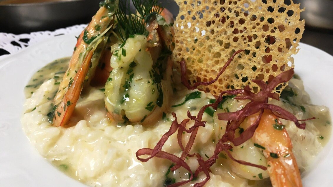 Ein köstliches Risotto mit Garnelen und einem knusprigen Biskuit. Das Gericht ist mit frischen Kräutern und Röstzwiebeln garniert. | © GH Großschedl zum Kramerwirt