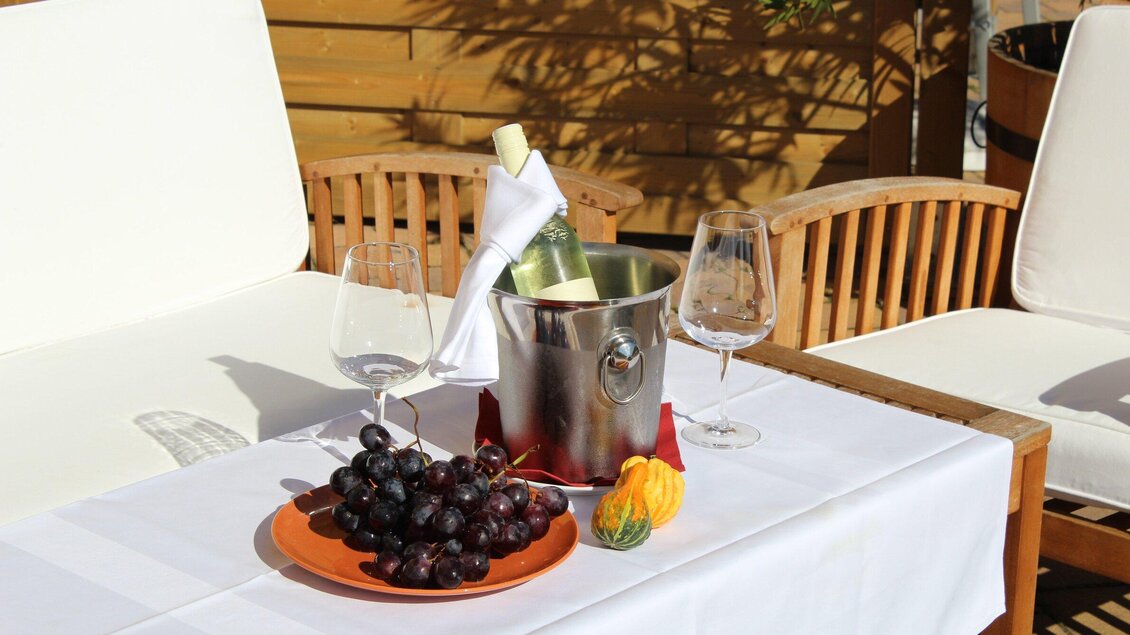 Ein eleganter Tisch mit einer Flasche Sekt in einem Kühlbehälter, zwei Weingläsern und einer Schale mit Trauben. Die Umgebung ist hell und einladend, ideal für eine entspannte Auszeit. | © Großschedl