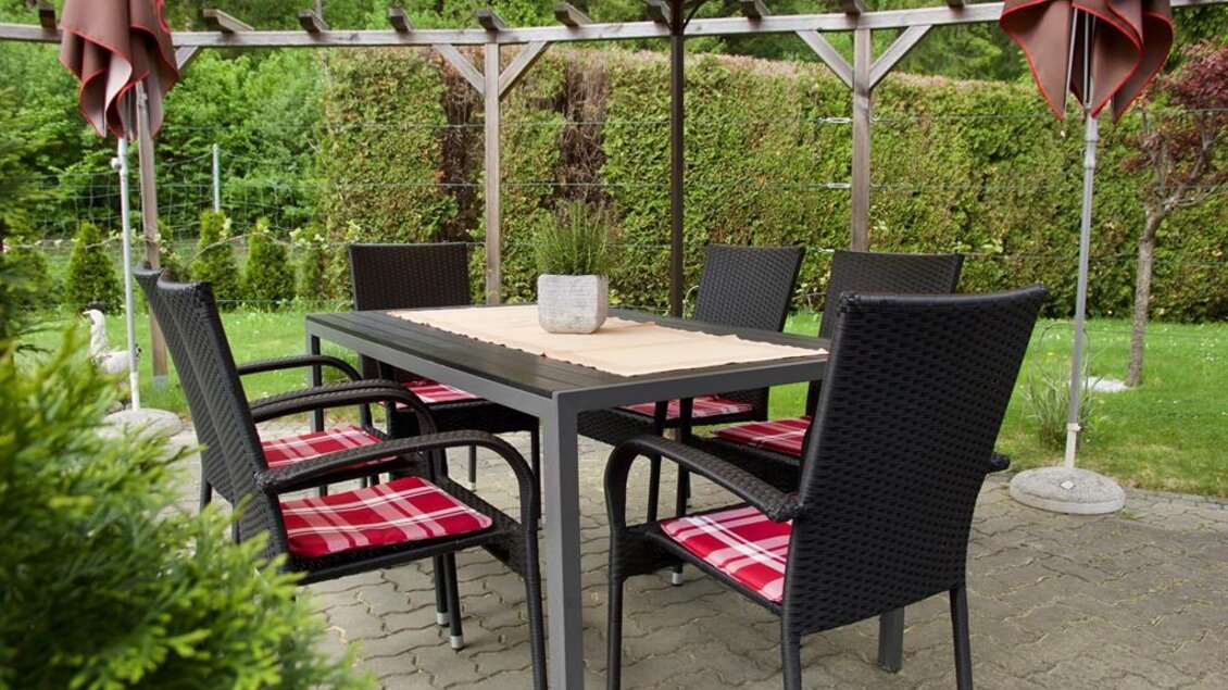 Ein gemütlicher Essbereich im Freien mit einem Tisch und schwarzen Stühlen. Der Bereich ist mit einem Sonnenschirm und einer grünen Hecke umgeben. | © Rainer M. Fürstaller