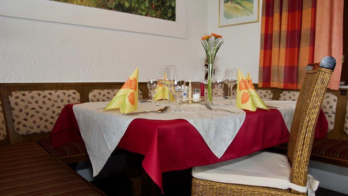 Ein gedeckter Tisch in einem gemütlichen Restaurant. Die Tischdecke ist rot und weiß, mit dekorativen Servietten und frischen Blumen. | © Rainer M. Fürstaller