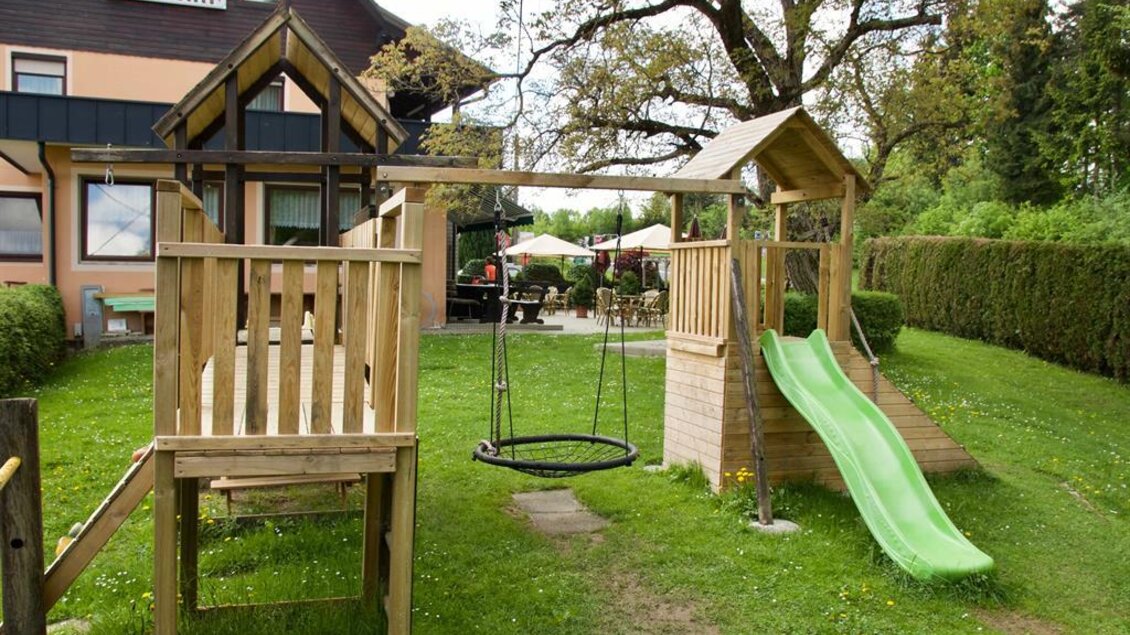 Ein Spielplatz mit einer Rutsche und einer Schaukel in einem Garten. Im Hintergrund sind Bäume und ein Gebäude zu sehen. | © Rainer M. Fürstaller