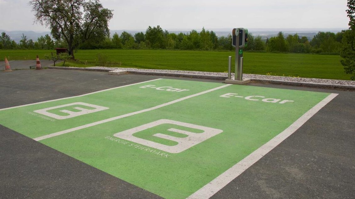 Ein Parkplatz für Elektroautos mit grünem Markierungssymbol. Im Hintergrund ist eine grüne Landschaft zu sehen. | © Rainer M. Fürstaller