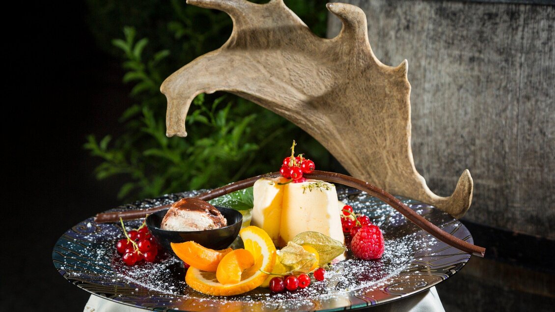 Ein schön angerichteter Dessertteller mit Eiskugel, Früchten und einem Stück Käse. Im Hintergrund ist ein Geweih sichtbar, das dem Bild einen rustikalen Charme verleiht. | © TV Region Graz - René Vidalli