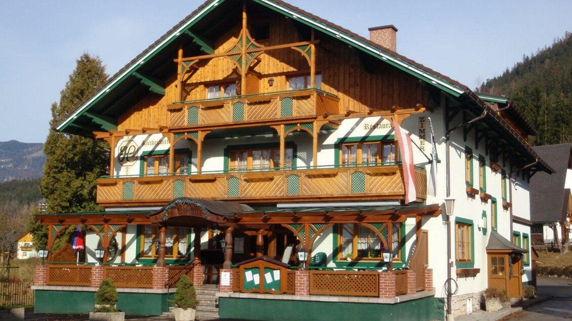 Ein traditionelles, mehrstöckiges Gebäude mit Holzverzierungen im alpenländischen Stil. Es bietet einen charmanten Außenbereich mit Blumen und Bäumen. | © Hilde Ladreiter