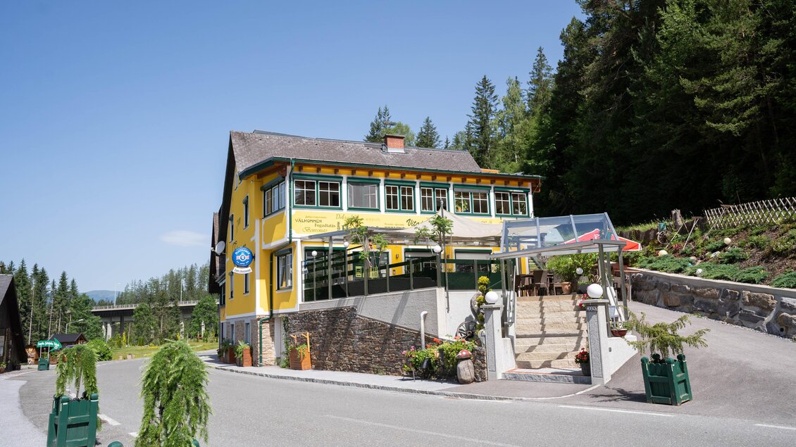 Ein gelbes Gebäude mit einem Restaurant und einer Terrasse. Es befindet sich an einer Straße, umgeben von Bäumen und Natur. | © Kump