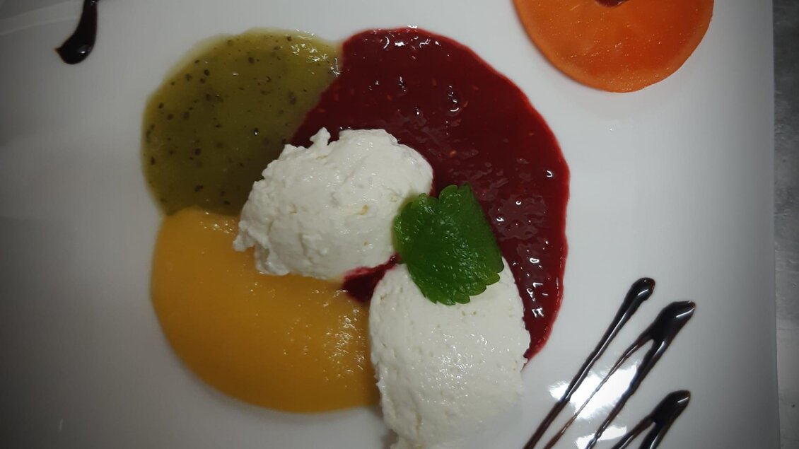 Ein kunstvoll angerichteter Teller mit drei Kugeln Eis und bunten Fruchtsoßen. Auf der Seite sind Schokoladengitter und eine orangefarbene Frucht dekoriert. | © Gasthof Klug Essen2 (c) Gasthof Klug-Klug