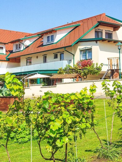 A charming building with red roofs and blooming flowers. In the foreground, there are green vines on a well-maintained lawn. | © Gasthof Knappenwirt