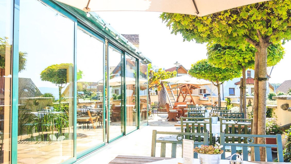 Eine helle und einladende Terrasse mit modernen Möbeln und Sonnenschirmen. Umgeben von Bäumen und Pflanzen, bietet sie einen schönen Ausblick und eine entspannte Atmosphäre. | © Gasthof Knappenwirt