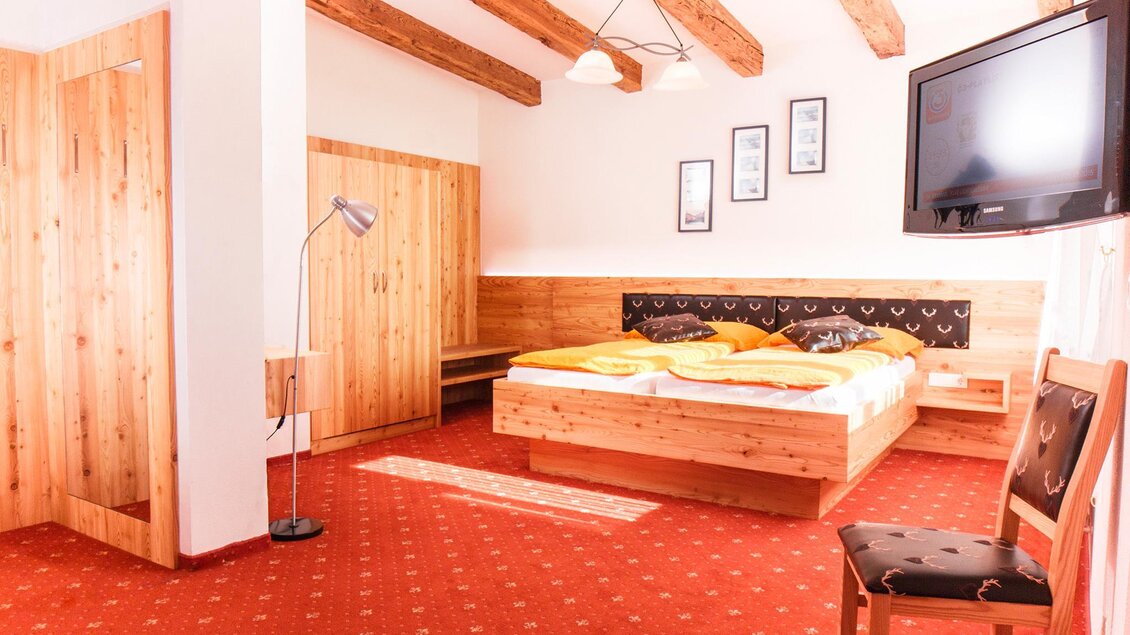 Ein helles Schlafzimmer mit Holzdekor und einem großen Bett. Der Raum hat einen Fernseher und eine gemütliche Atmosphäre. | © Gasthof Knappenwirt