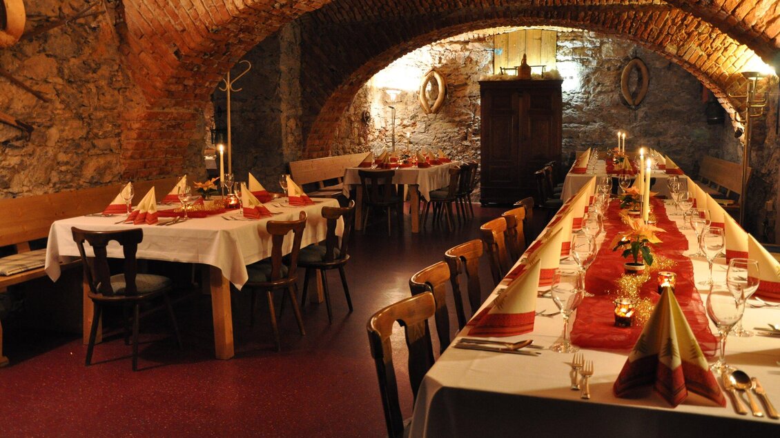 Ein stilvolles Restaurant mit einem gewölbten Steinraum. Die Tische sind festlich gedeckt mit roten Servietten und Kerzen. | © TV Region Graz - Lunghammer