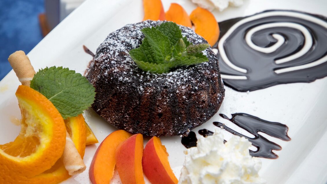 Eine köstliche Schokoladentorte auf einem weißen Teller, garniert mit frischen Früchten und Schlagsahne. Die Dekoration umfasst Schokoladensauce und frische Minze. | © TV Region Graz - Lunghammer