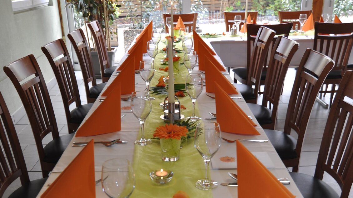 Ein schön gedeckter Tisch mit orangefarbenen Servietten und einer grünen Tischdecke. In der Mitte sind Blumen und Kerzen dekoriert. | © TV Region Graz - Lunghammer