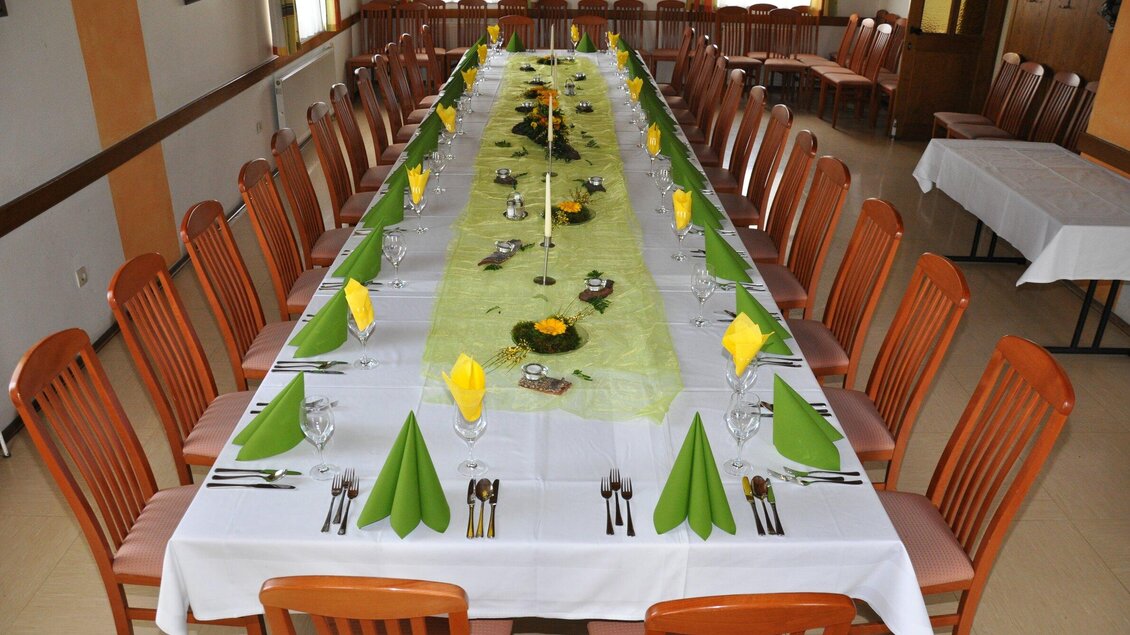 Ein festlich gedeckter Tisch mit einer langen weißen Tischdecke und grünen Servietten. Daneben stehen viele Stühle, die auf Gäste warten. | © TV Region Graz - Lunghammer