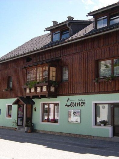 Ein charmantes Gästehaus mit einer Holzfassade und grün gestrichener Unterseite. Vor dem Gebäude sind Parkplätze vorhanden und die Umgebung ist von Bäumen umgeben. | © Barbara Leuner