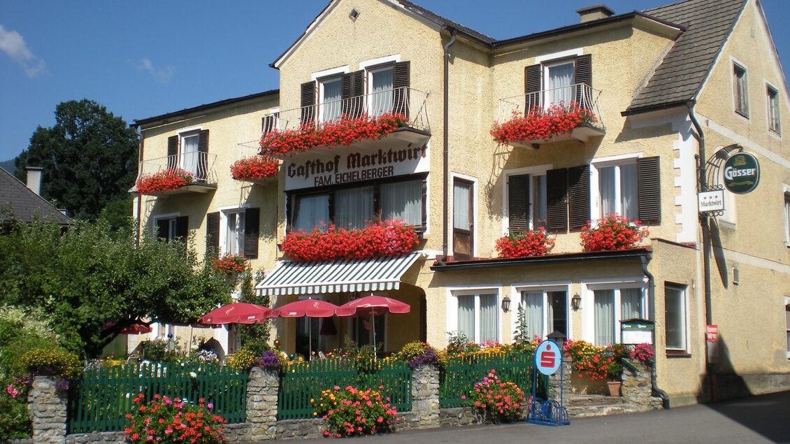Ein charmantes Gasthaus mit blühenden Balkonkästen. Der Eingangsbereich ist von bunten Blumen umgeben und lädt zum Verweilen ein.
